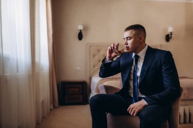 Takım elbiseli genç ve yakışıklı bir adam cam tutuyor ve odada oturuyor. 