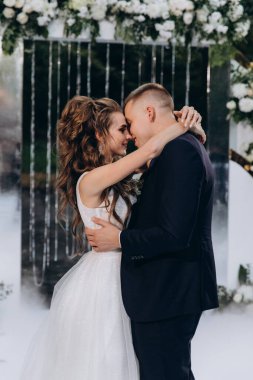 Güzel, mutlu, genç bir çift. Dekoratif çiçek kemerinin yanında dans ediyorlar.          