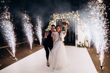 Mutlu gelin ve damat parkta düğün kemerinin yanında poz veriyor.          