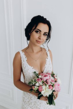 Beyaz elbiseli güzel genç gelin zarif iç kısımda düğün buketi ile poz veriyor.          
