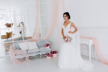 Beyaz elbiseli güzel genç gelin zarif iç kısımda düğün buketi ile poz veriyor.          