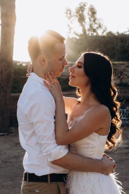 Genç bir çift düğün günlerinde güneşli bir yaz parkında romantik bir anın tadını çıkarır. Doğayla çevrili, gülümsüyor ve birbirlerine sevgiyle sarılıyorlar..