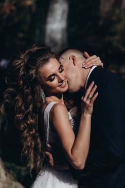 Genç bir çift düğün günlerinde güneşli bir yaz parkında romantik bir anın tadını çıkarır. Doğayla çevrili, gülümsüyor ve birbirlerine sevgiyle sarılıyorlar..