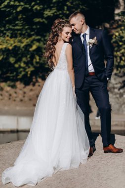 Genç bir çift düğün günlerinde güneşli bir yaz parkında romantik bir anın tadını çıkarır. Doğayla çevrili, gülümsüyor ve birbirlerine sevgiyle sarılıyorlar..