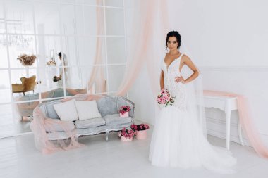 Beyaz elbiseli güzel genç gelin zarif iç kısımda düğün buketi ile poz veriyor.          