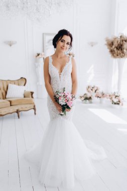 Beyaz elbiseli güzel genç gelin zarif iç kısımda düğün buketi ile poz veriyor.          