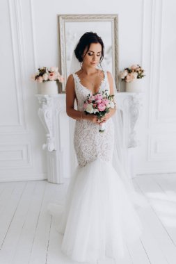 Beyaz elbiseli güzel genç gelin zarif iç kısımda düğün buketi ile poz veriyor.          