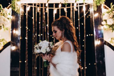 Genç ve güzel bir gelin, özel gününde göz kamaştırıcı düğün süslerinin önünde zarifçe poz verir..