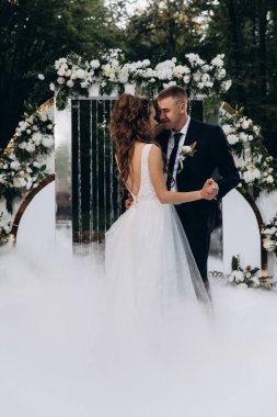 Güzel, mutlu, genç bir çift. Dekoratif çiçek kemerinin yanında dans ediyorlar.          