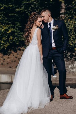 Genç bir çift düğün günlerinde güneşli bir yaz parkında romantik bir anın tadını çıkarır. Doğayla çevrili, gülümsüyor ve birbirlerine sevgiyle sarılıyorlar..