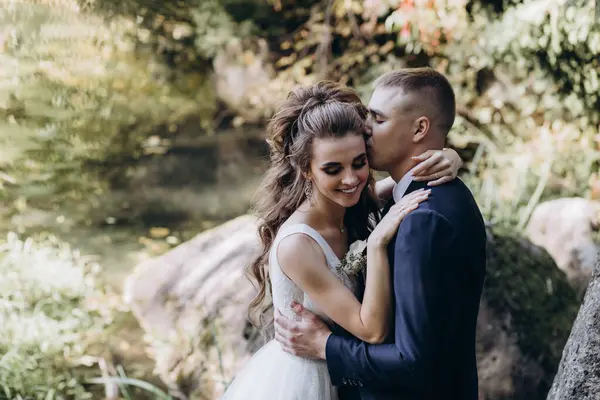 Genç bir çift düğün günlerinde güneşli bir yaz parkında romantik bir anın tadını çıkarır. Doğayla çevrili, gülümsüyor ve birbirlerine sevgiyle sarılıyorlar..