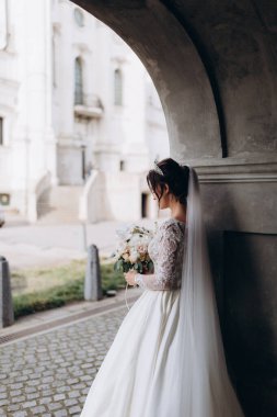 Gelinlik giymiş genç bir gelin eski kasabada elinde bir buket çiçek tutuyor..       