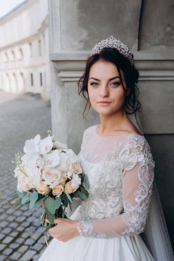 Gelinlik giymiş genç bir gelin eski kasabada elinde bir buket çiçek tutuyor..       