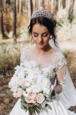 Gelinlik ve duvak içinde güzel bir gelin Ormanda bir buket çiçek tutuyor              