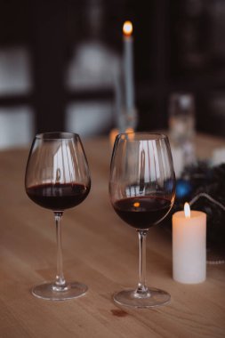 Ahşap masada iki kadeh kırmızı şarap ve mum.