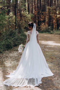 Gelinlik ve duvak içinde güzel bir gelin Ormanda bir buket çiçek tutuyor              