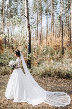 Gelinlik ve duvak içinde güzel bir gelin Ormanda bir buket çiçek tutuyor              