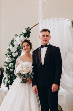 Mutlu gelin ve damat düğün kemerinin yanında yan yana durur.