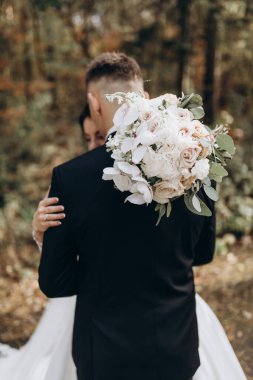 Güzel mutlu gelin ve damat düğün günü ormanda birbirlerine sarılıp poz veriyorlar.                            