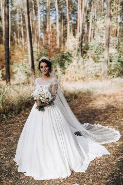 Gelinlik ve duvak içinde güzel bir gelin Ormanda bir buket çiçek tutuyor              