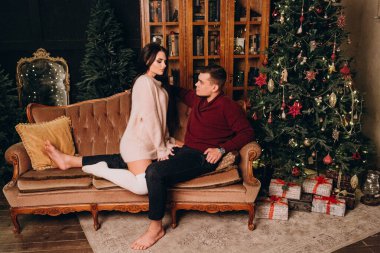 Stüdyoda rahat bir Noel süslemesi ile kanepede poz veren birbirine aşık genç bir çift. Yeni yılın aşk hikayesi.. 