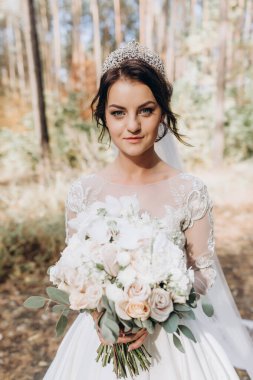 Gelinlik ve duvak içinde güzel bir gelin Ormanda bir buket çiçek tutuyor              