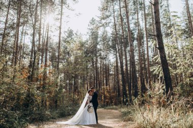 Güzel mutlu gelin ve damat düğün günü ormanda birbirlerine sarılıp poz veriyorlar.                            