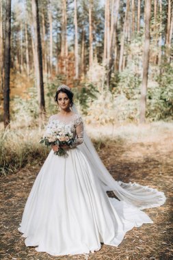 Gelinlik ve duvak içinde güzel bir gelin Ormanda bir buket çiçek tutuyor              