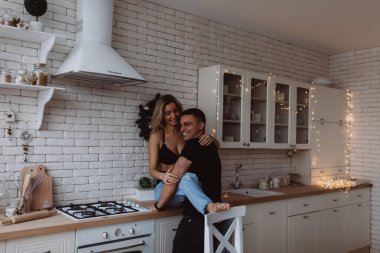 Arka planda Noel süsleri olan güzel bir çift mutfakta poz verirken gülüyor.