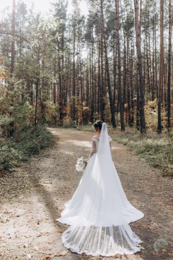 Gelinlik ve duvak içinde güzel bir gelin Ormanda bir buket çiçek tutuyor              
