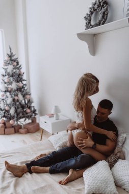Birbirine aşık çiftler, yatakta şehvetle poz veriyorlar. Yılbaşı dekorasyonları var.