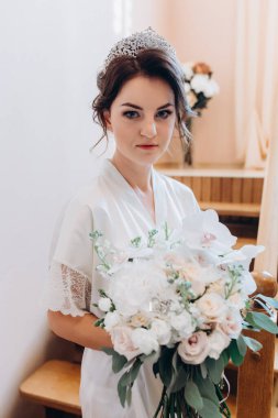 Beyaz bornozlu güzel gelin elinde buketle kameraya bakıyor.