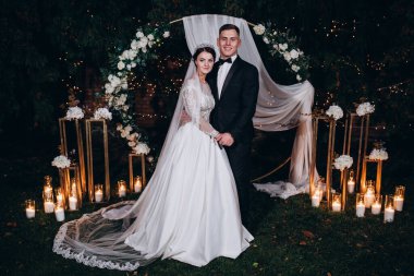 Gelin ve damat düğün kemerinde düğün süsleriyle dikiliyorlar.