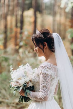 Gelinlik ve duvak içinde güzel bir gelin Ormanda bir buket çiçek tutuyor              