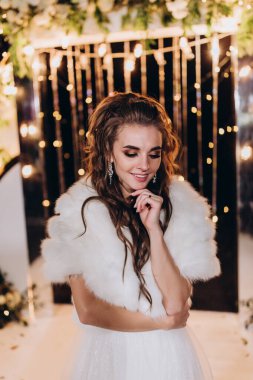 Genç ve güzel bir gelin, özel gününde göz kamaştırıcı düğün süslerinin önünde zarifçe poz verir..