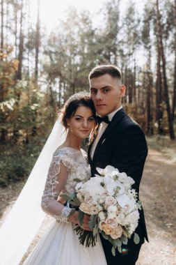 Güzel mutlu gelin ve damat düğün günü ormanda birbirlerine sarılıp poz veriyorlar.                            