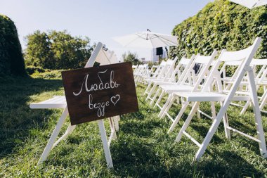 Parkta beyaz sandalyeli bir düğün töreni.