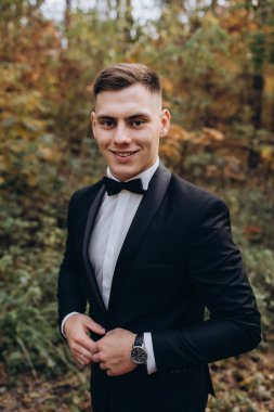 Gelinlik giymiş yakışıklı damat ormanda dikiliyor.    