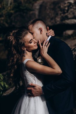 Genç bir çift düğün günlerinde güneşli bir yaz parkında romantik bir anın tadını çıkarır. Doğayla çevrili, gülümsüyor ve birbirlerine sevgiyle sarılıyorlar..