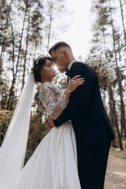 Güzel mutlu gelin ve damat düğün günü ormanda birbirlerine sarılıp poz veriyorlar.                            