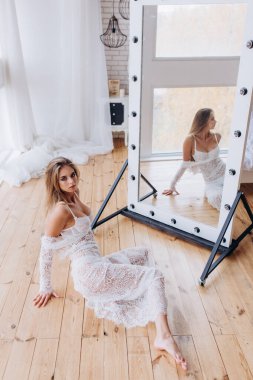 Genç ve güzel bir kız beyaz dantelli elbise ve iç çamaşırlarıyla aynada yansıyor.         