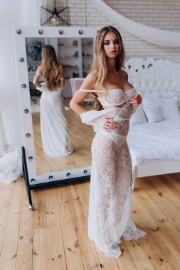 Genç ve güzel bir kız beyaz dantelli elbise ve iç çamaşırlarıyla aynada yansıyor.         