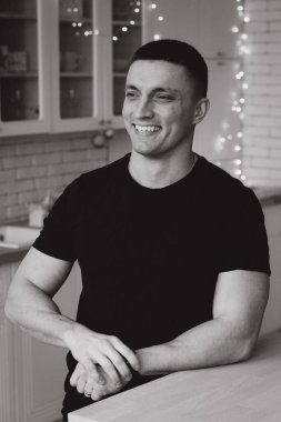 Mutfakta poz veren gülümseyen genç adam, tek renkli fotoğraf.