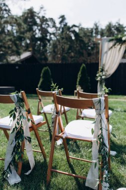 Düğün töreni için yeşil çimlerde yeşil yapraklarla süslenmiş boş sandalyeler.