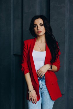 Kırmızı ceketli genç ve güzel bir kadın koyu bir arkaplanda poz veriyor.