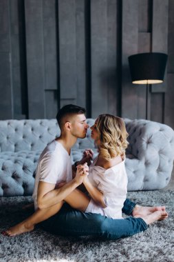 Stüdyoda gri kanepenin yanında birbirine aşık genç bir çift poz veriyor.