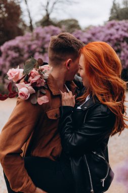 Genç ve güzel bir çift çiçek açan çalılara karşı poz veriyor. 