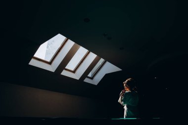 Beyaz cüppeli çekici bir kadın karanlık odada dikiliyor.    