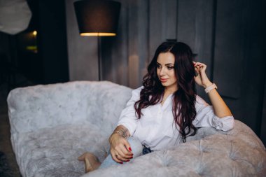 Stüdyoda gri koltukta poz veren güzel esmer kadın.