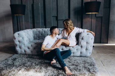 Stüdyoda gri koltukta poz veren genç ve güzel bir çift.